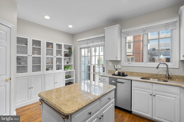 kitchen with white cabinetry, stainless steel dishwasher, sink, a kitchen island, and light stone counters