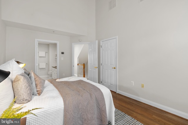 bedroom featuring ensuite bathroom, dark hardwood / wood-style floors, and a towering ceiling