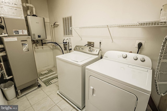 laundry area featuring water heater, light tile patterned floors, and washing machine and clothes dryer