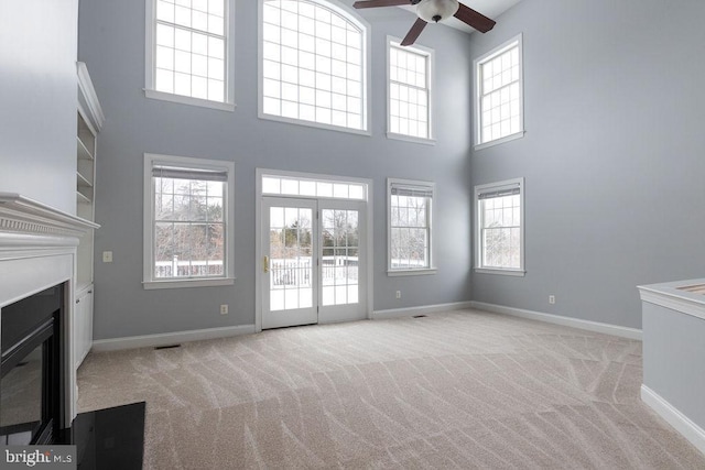 unfurnished living room with light carpet, a high ceiling, and ceiling fan