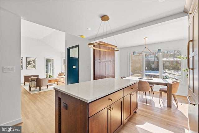 kitchen featuring a kitchen island, decorative light fixtures, lofted ceiling with beams, light wood-type flooring, and light stone counters