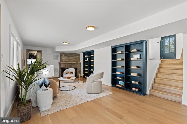 living area featuring hardwood / wood-style flooring, built in features, and a stone fireplace