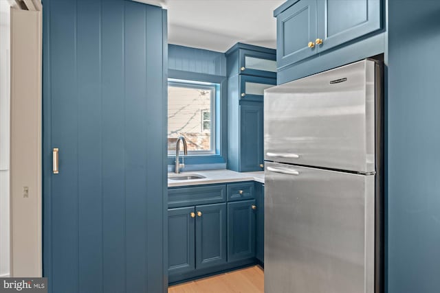 kitchen featuring light hardwood / wood-style floors, sink, blue cabinetry, and stainless steel refrigerator