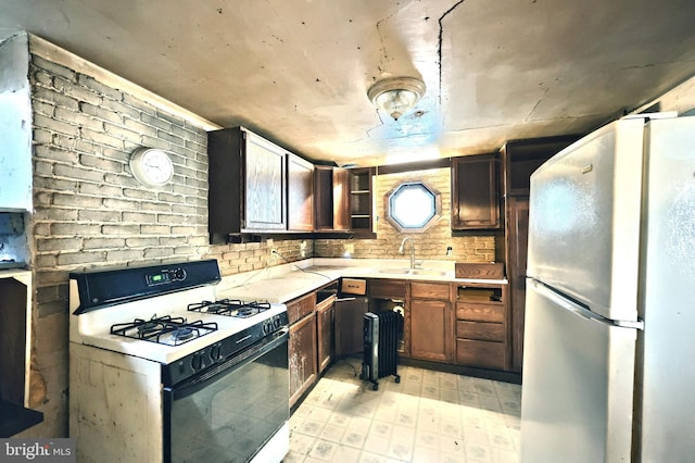 kitchen featuring sink, brick wall, gas range gas stove, and refrigerator