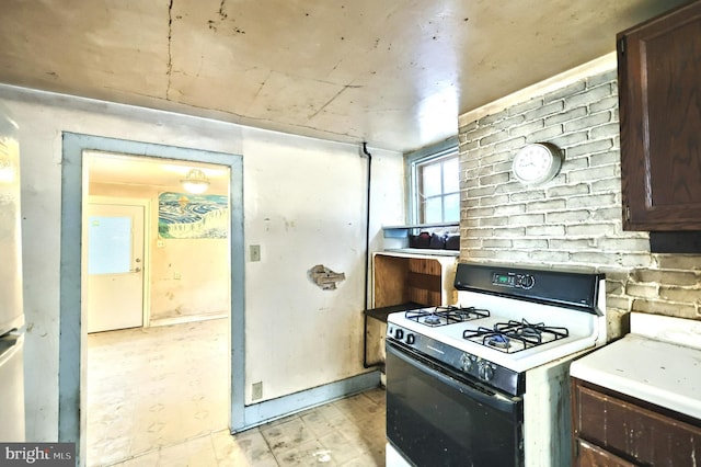 kitchen featuring dark brown cabinets, brick wall, and white range with gas cooktop