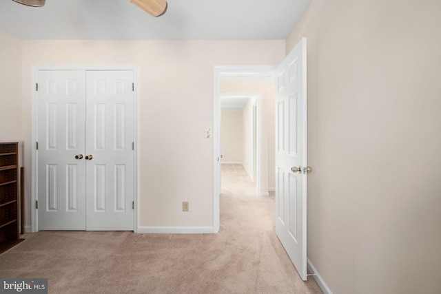 unfurnished bedroom featuring a closet, baseboards, and light colored carpet