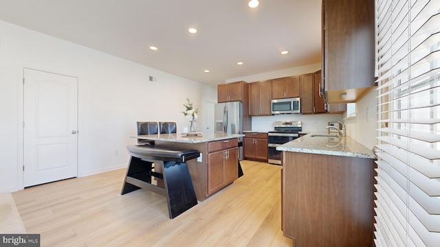 kitchen with a breakfast bar area, light wood-type flooring, a kitchen island, stainless steel appliances, and light stone countertops