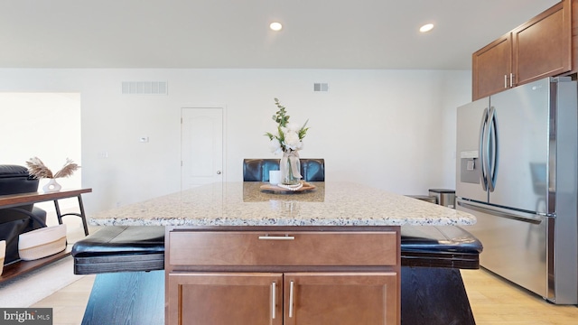 kitchen with stainless steel fridge, light stone countertops, light hardwood / wood-style floors, and a kitchen island