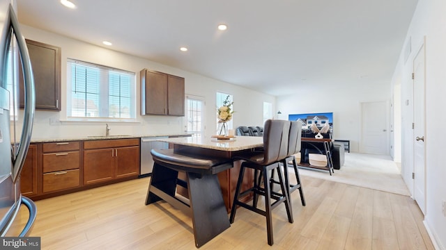 kitchen featuring sink, a breakfast bar area, stainless steel appliances, light stone countertops, and light wood-type flooring