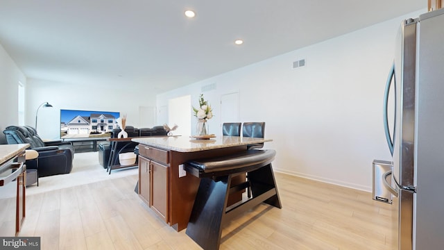 kitchen with light stone counters, light hardwood / wood-style flooring, stainless steel fridge, a kitchen breakfast bar, and a kitchen island