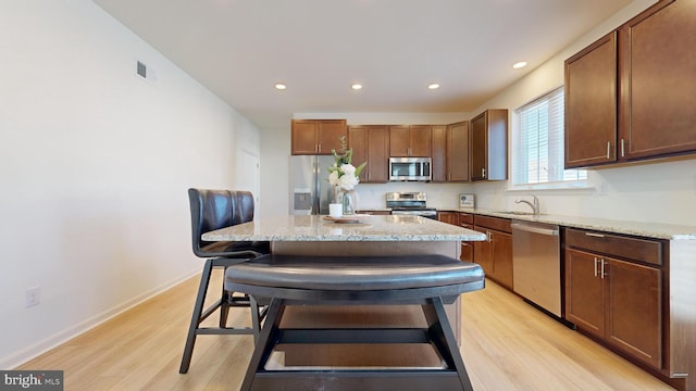 kitchen featuring stainless steel appliances, light stone countertops, a kitchen island, and a kitchen breakfast bar