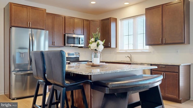 kitchen with a kitchen bar, sink, appliances with stainless steel finishes, a kitchen island, and light hardwood / wood-style floors