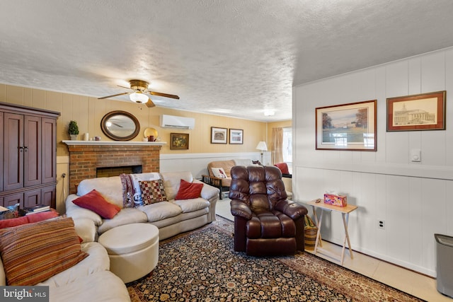 living room with an AC wall unit, tile patterned flooring, ceiling fan, a brick fireplace, and a textured ceiling