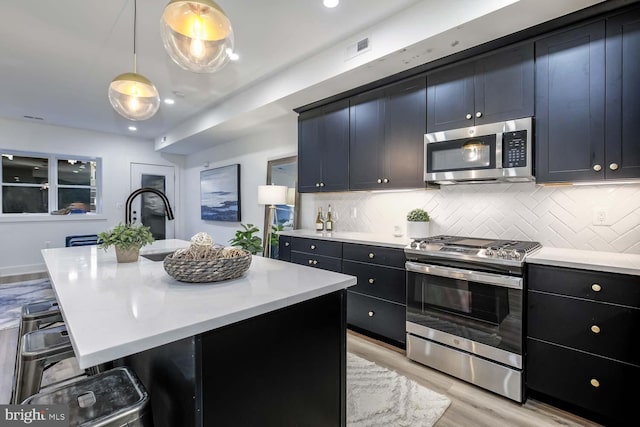 kitchen featuring decorative light fixtures, a kitchen island with sink, appliances with stainless steel finishes, and a breakfast bar