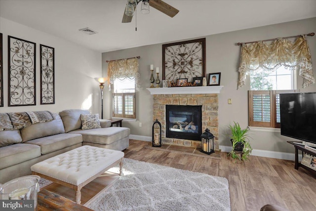 living room with hardwood / wood-style flooring, ceiling fan, and a stone fireplace