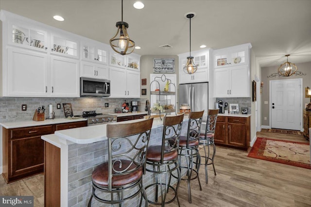 kitchen with appliances with stainless steel finishes, a kitchen island with sink, hanging light fixtures, white cabinetry, and light hardwood / wood-style floors