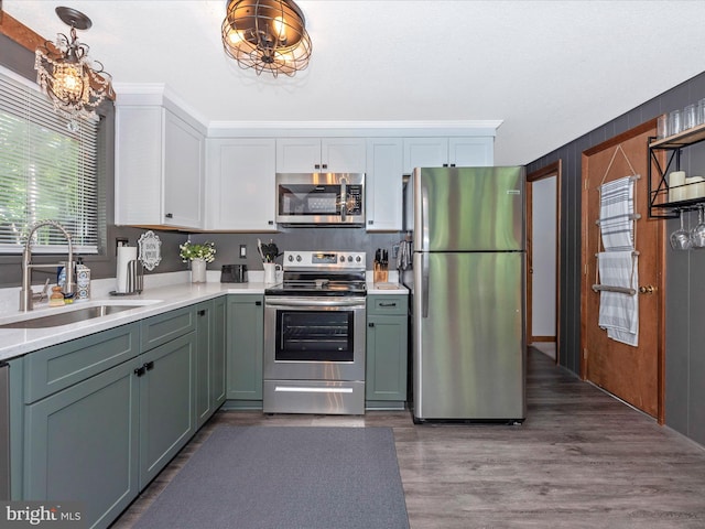 kitchen with sink, wood-type flooring, decorative light fixtures, stainless steel appliances, and white cabinets