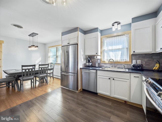 kitchen featuring white cabinets, appliances with stainless steel finishes, dark hardwood / wood-style flooring, sink, and hanging light fixtures