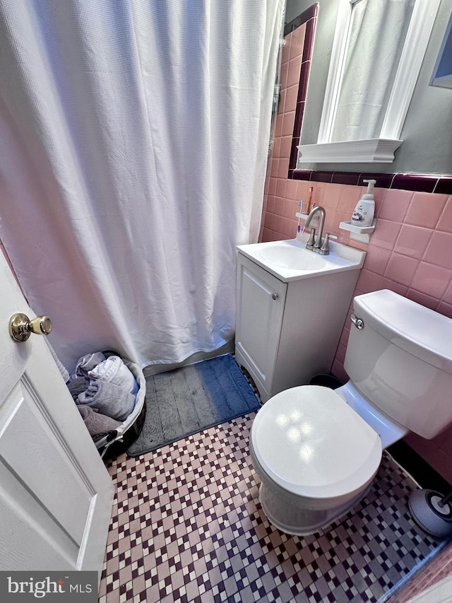 bathroom featuring toilet, tile patterned flooring, vanity, and tile walls