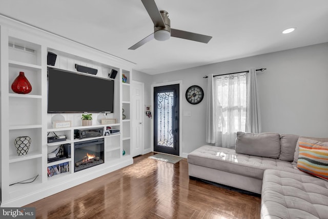 living room with built in shelves, hardwood / wood-style flooring, and ceiling fan