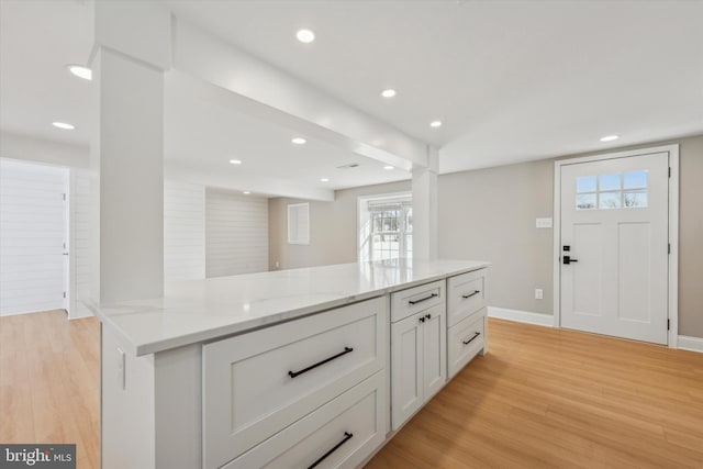 kitchen featuring a kitchen island, white cabinetry, light hardwood / wood-style flooring, and light stone countertops