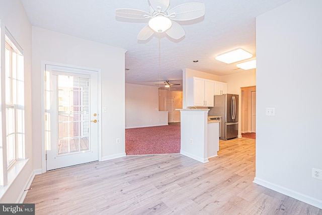 interior space featuring white cabinetry, stainless steel fridge, kitchen peninsula, ceiling fan, and light hardwood / wood-style flooring