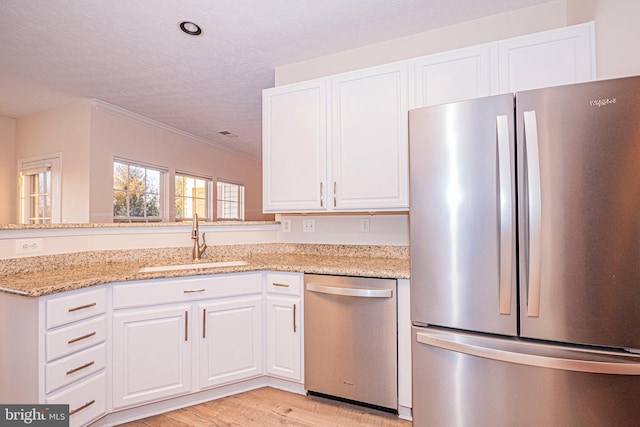 kitchen with sink, white cabinets, light wood-type flooring, light stone countertops, and stainless steel appliances