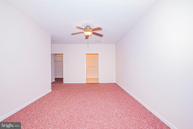 unfurnished bedroom with ceiling fan, a textured ceiling, carpet floors, a spacious closet, and a closet