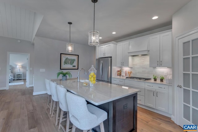 kitchen with decorative light fixtures, a kitchen island with sink, white cabinetry, and stainless steel appliances