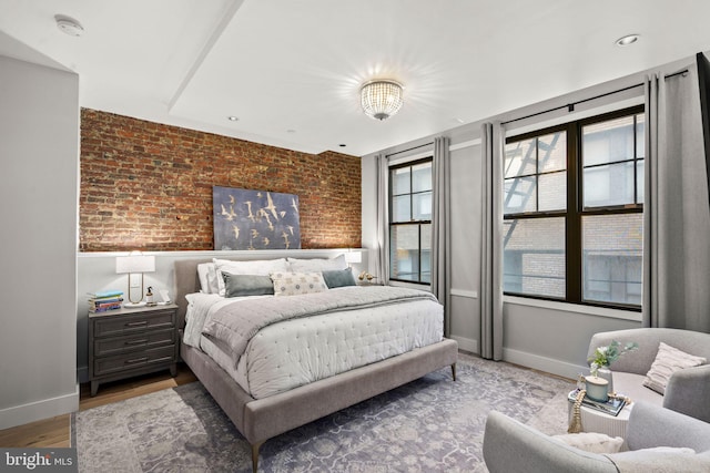 bedroom featuring wood-type flooring and brick wall