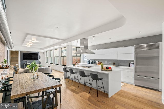 kitchen with light hardwood / wood-style flooring, white cabinetry, built in refrigerator, a kitchen bar, and island range hood