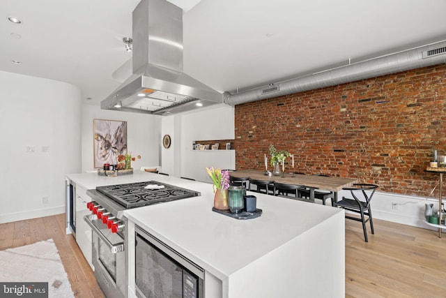 kitchen featuring brick wall, appliances with stainless steel finishes, a kitchen island, island range hood, and light hardwood / wood-style flooring