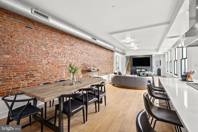 dining space featuring brick wall and light hardwood / wood-style flooring