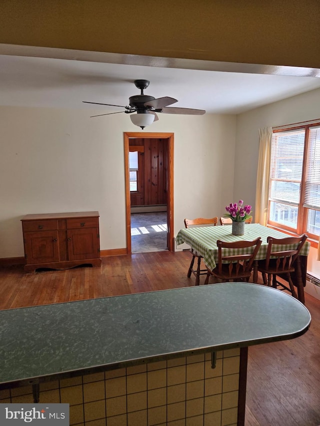 dining room featuring a ceiling fan, baseboards, a baseboard heating unit, and wood finished floors