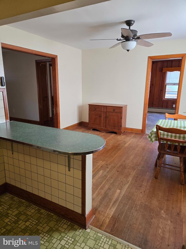 interior space with a baseboard heating unit, a ceiling fan, baseboards, and wood finished floors