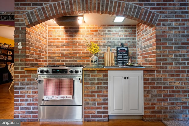 kitchen with hardwood / wood-style flooring, brick wall, white cabinets, and stainless steel gas range oven