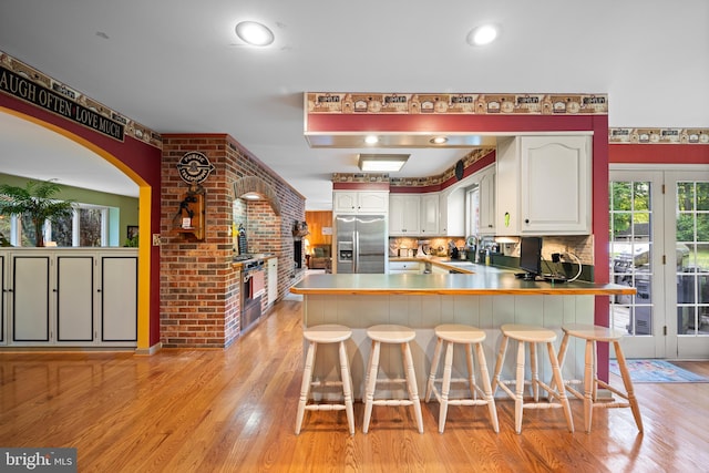 kitchen featuring stainless steel fridge with ice dispenser, white cabinetry, kitchen peninsula, and a breakfast bar area