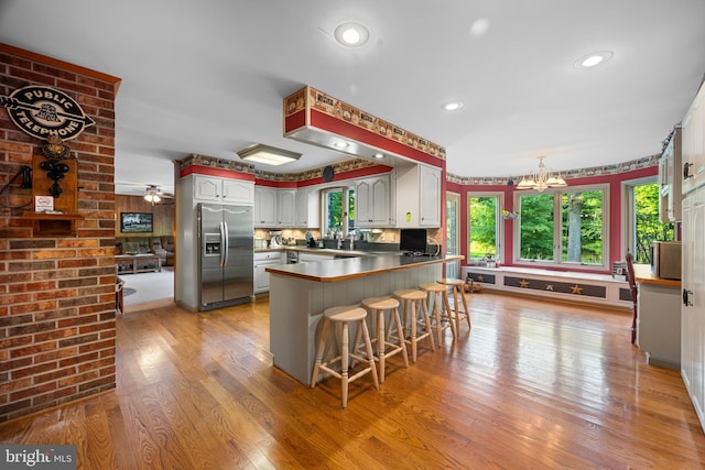 kitchen with a kitchen bar, light hardwood / wood-style floors, stainless steel fridge with ice dispenser, white cabinetry, and kitchen peninsula