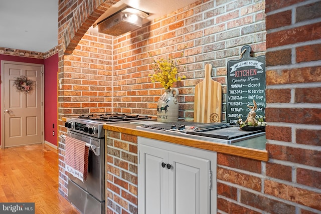 kitchen featuring exhaust hood, brick wall, gas range, white cabinets, and light hardwood / wood-style flooring