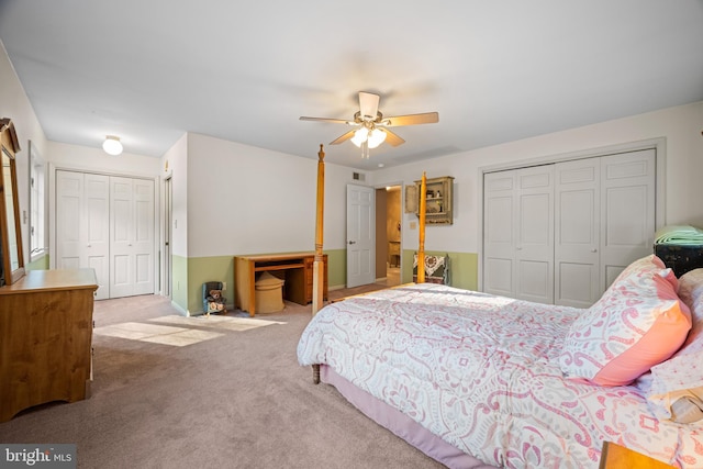 bedroom with ceiling fan, light colored carpet, and two closets