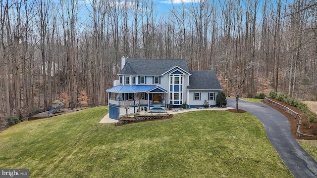 view of front of property with a front lawn, driveway, a view of trees, a porch, and a chimney