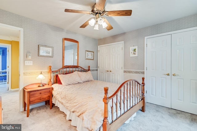 bedroom with wallpapered walls, light colored carpet, multiple closets, and a ceiling fan