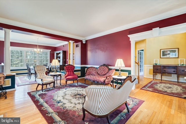 living area featuring an inviting chandelier, crown molding, wood finished floors, and ornate columns