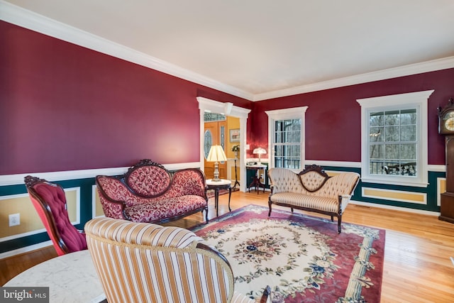 living area featuring a wainscoted wall, wood finished floors, and crown molding