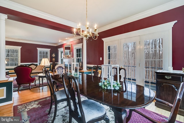 dining room with a notable chandelier, wood finished floors, crown molding, and ornate columns