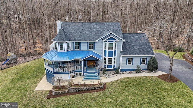 view of front of house featuring aphalt driveway, a porch, a front yard, a shingled roof, and a chimney