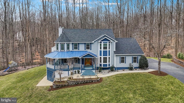 view of front of home with a front lawn, driveway, a porch, metal roof, and a chimney