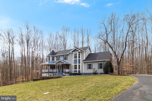 view of front of home featuring aphalt driveway, a front lawn, a porch, and a chimney