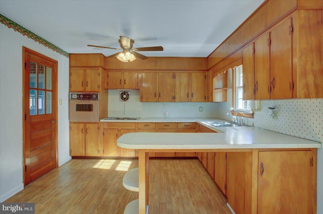 kitchen with stainless steel oven, light hardwood / wood-style floors, sink, gas cooktop, and kitchen peninsula