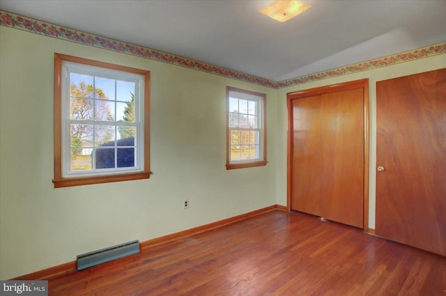 unfurnished bedroom with hardwood / wood-style flooring, a baseboard radiator, multiple windows, and a closet